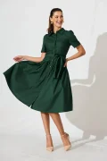 Woman in a dark green belted dress twirling, wearing nude heels and gold earrings, smiling.