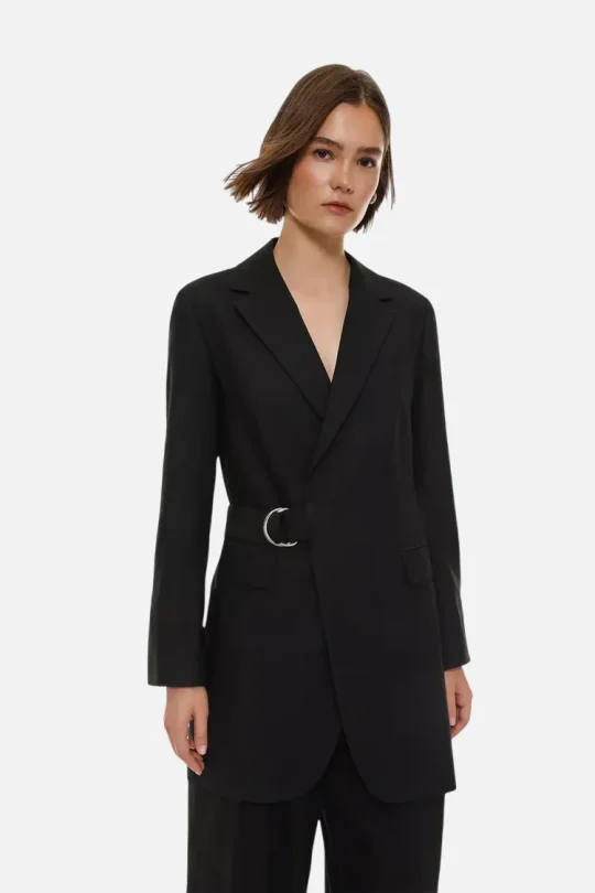 Woman wearing a black tailored blazer with a silver-buckle belt over matching black pants on a neutral background.