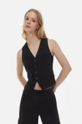 Woman wearing a black sleeveless vest with a button-front design over matching black pants, posed against a white background.
