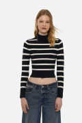 Model wearing a navy and white striped cropped knit turtleneck sweater paired with blue jeans, facing forward.