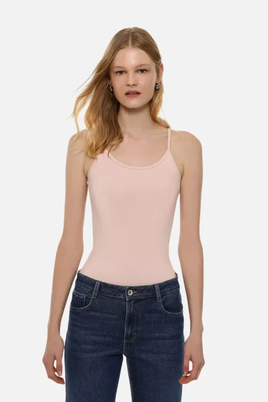 Woman wearing a light pink sleeveless tank top tucked into dark blue jeans, standing facing the camera against a white background.