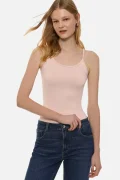 Woman wearing a pale pink sleeveless camisole and dark blue jeans, posing with one hand at her waistband against a white background.