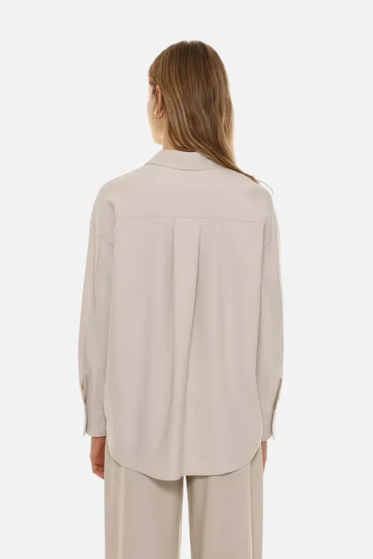 Back view of a person wearing a loose beige shirt and matching wide-leg pants, hair down and small hoop earrings visible.